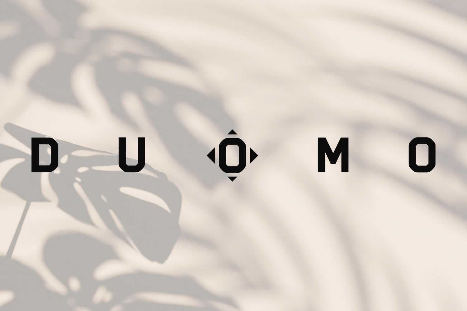 The word "DUOMO" with tropical leaves casting shadows in the background.